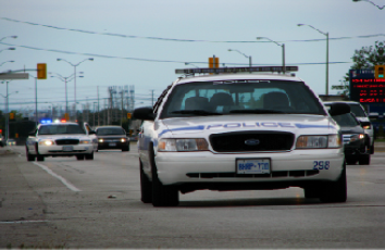 A photograph shows two police cars driving, one with its lights flashing.