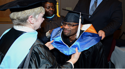 A photograph shows several people gathered outdoors wearing caps and gowns in a graduation ceremony.