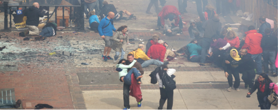 A photograph shows a crowd at the site of the Boston Marathon bombing immediately after it occurred. Debris is scattered on the ground, several people appear to be injured, and several people are helping others.