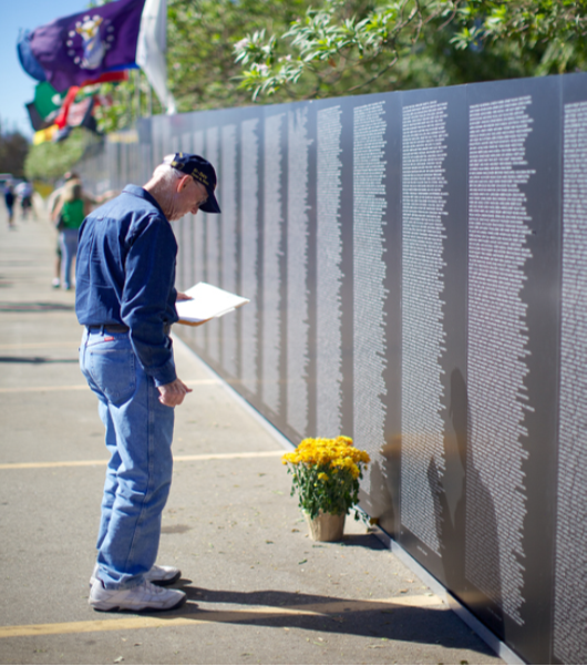 A photograph shows a person looking at the Vietnam Traveling Memorial Wall.
