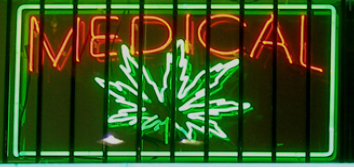 A photograph shows a window with a neon sign. The sign includes the word “medical” above the shape of a marijuana leaf.