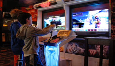 A photograph shows two children playing a video game and pointing a gun-like object toward a screen.
