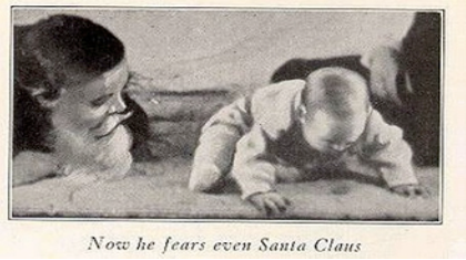 A photograph shows a man wearing a mask with a white beard; his face is close to a baby who is crawling away. A caption reads, “Now he fears even Santa Claus.”
