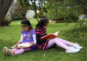 Children sitting on grass and reading.