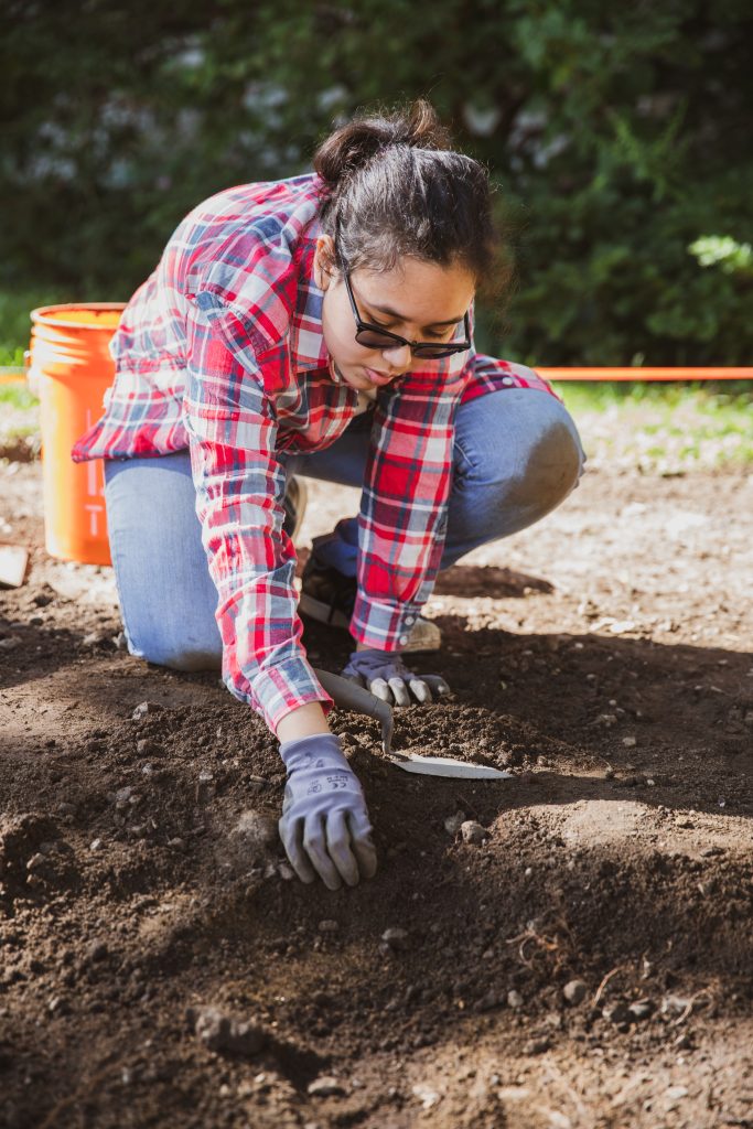 Image of a student on an archeology dig on campus.