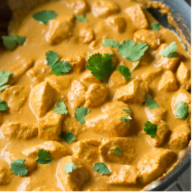 Chunks of chicken swimming in light brown creamy sauce with green cilantro leaves sprinkled o top.