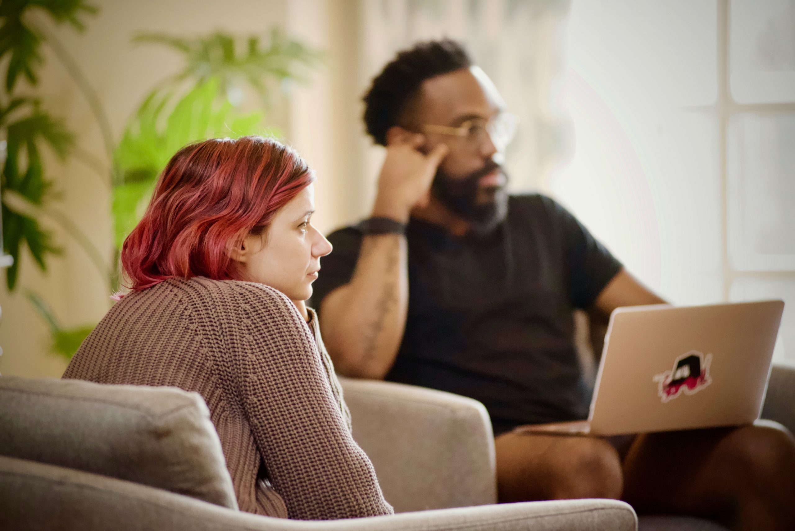 a young white woman and a young Black man with a laptop are seated listening to a speaker outside the frame of the image