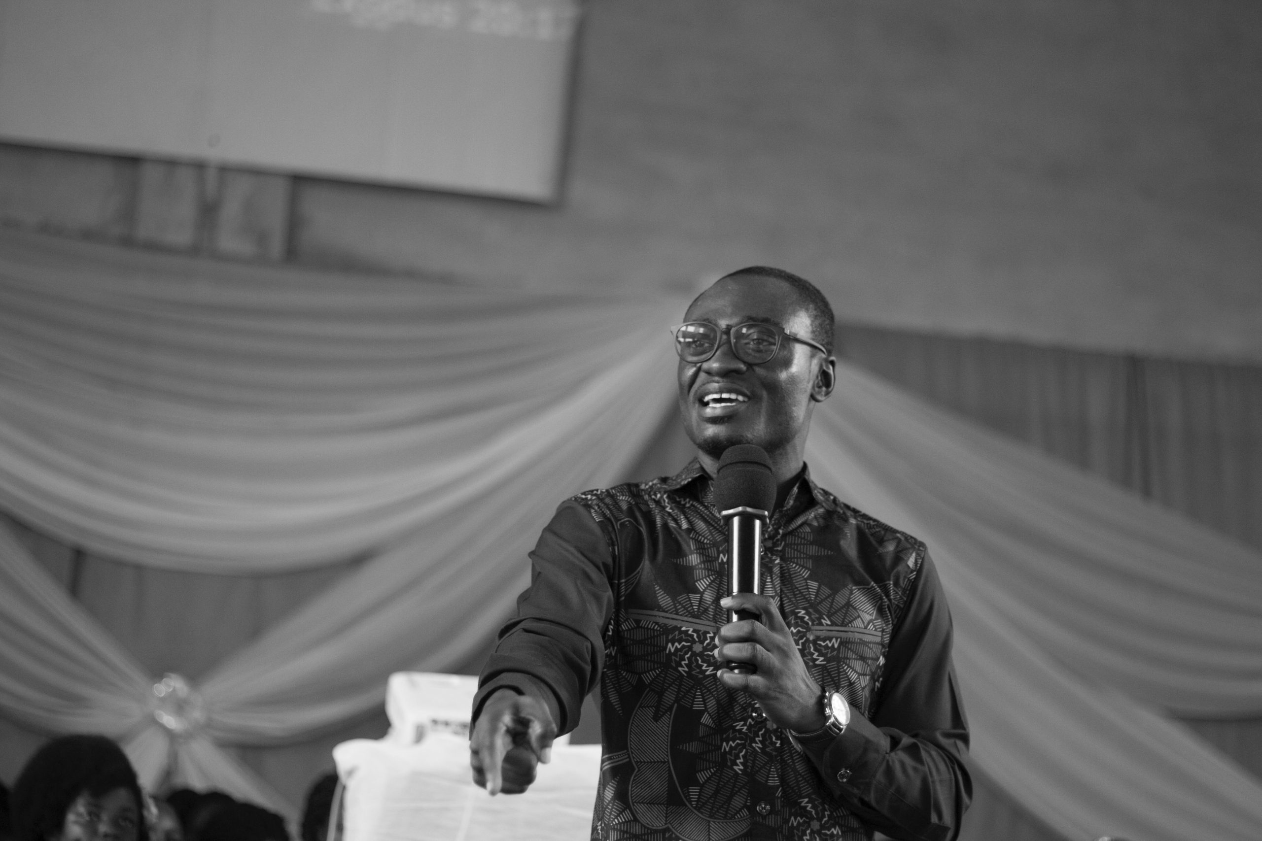 a Black man speaking into a microphone in what appears to be an auditorium