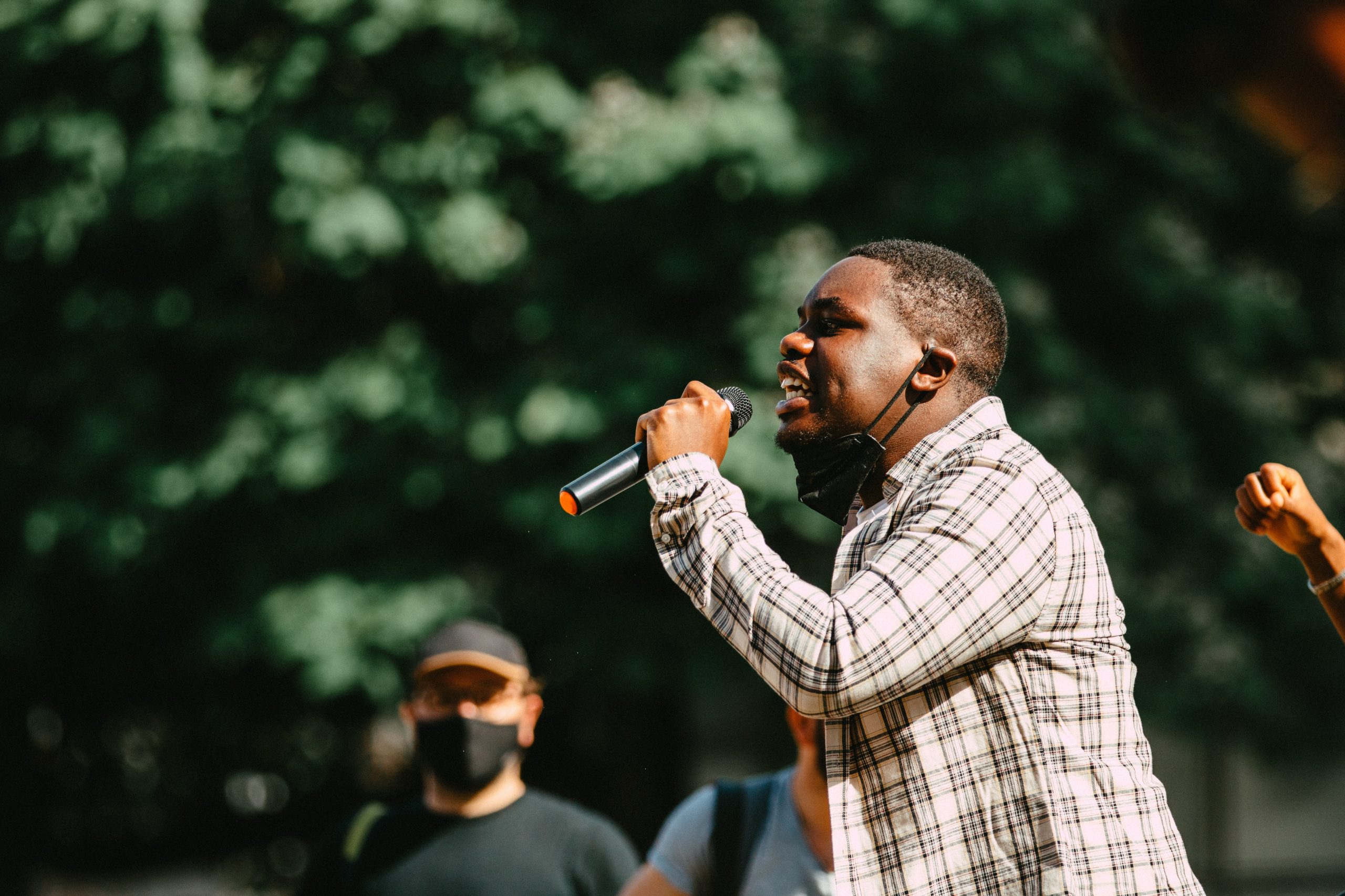 a Black man speaking into a microphone at an outdoor assembly