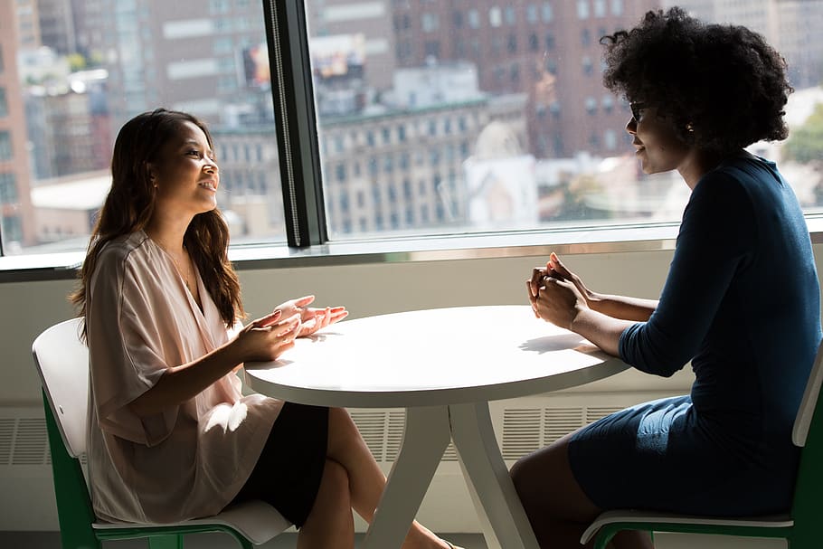 Two women chatting at desk (One Asian and one African American)