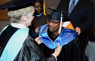 Black man receiving his doctoral hood as part as a graduation ceremony