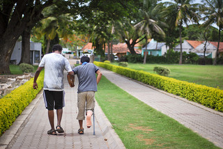 A young man helping another with crutches and a leg in a cast