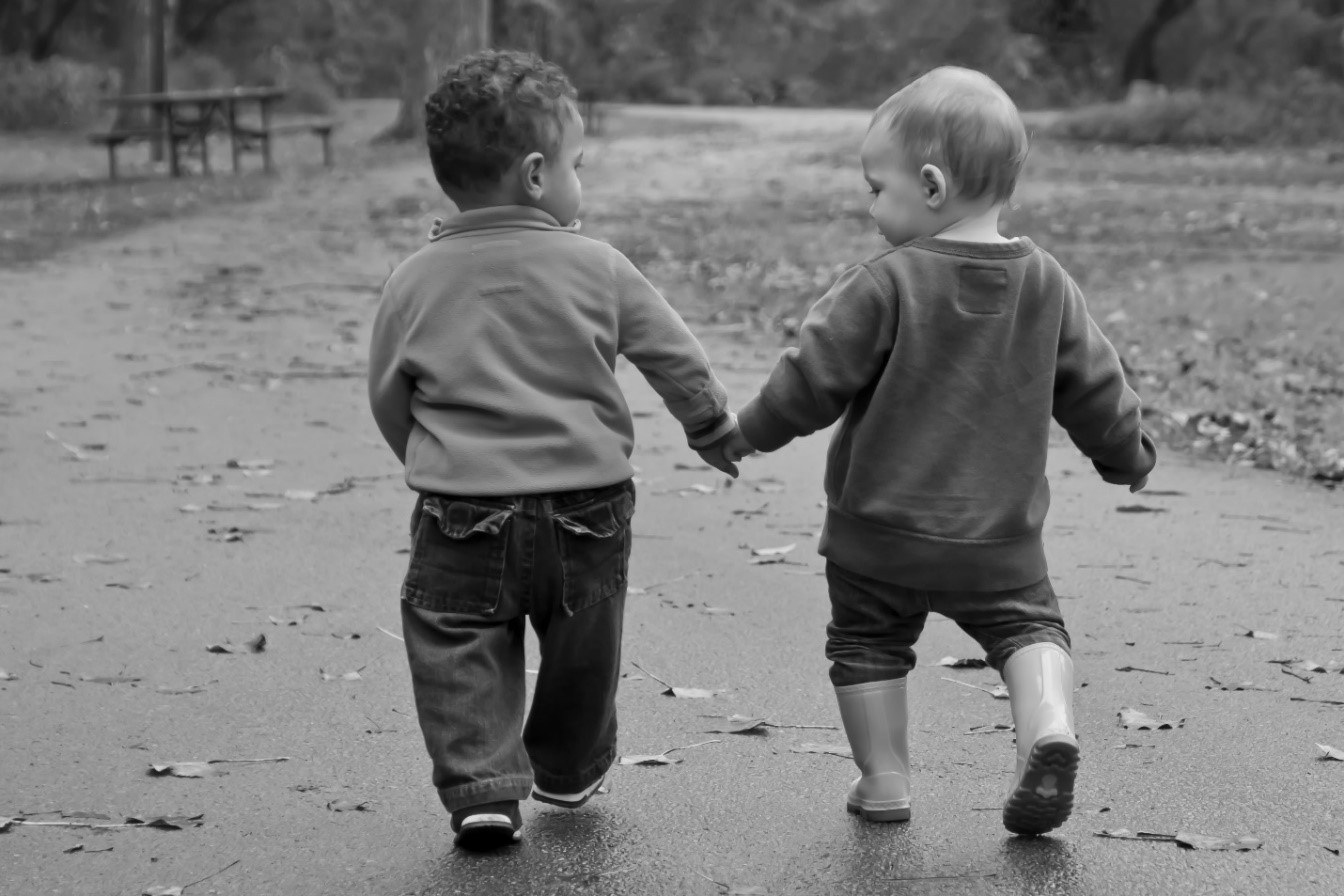 Two toddlers walking in the park holding hands and looking at each other