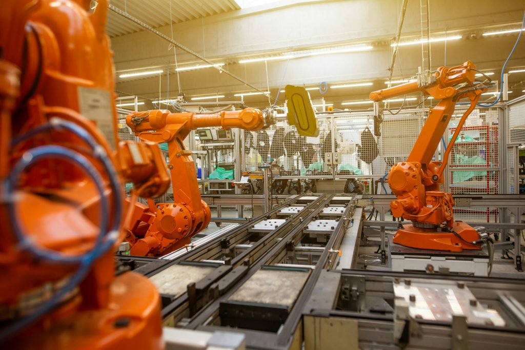 a factory scene with big orange robotic assembly machinery, with one barely visible worker in background