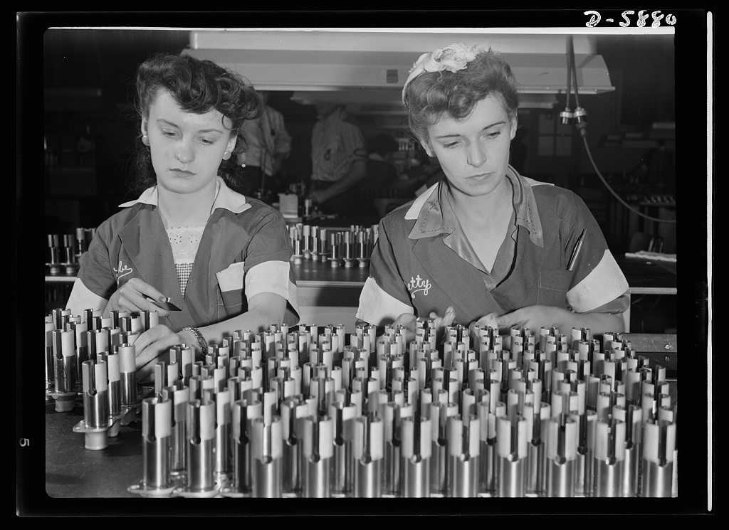 two young 'Rosie the riveters' inspecting airplane motor parts