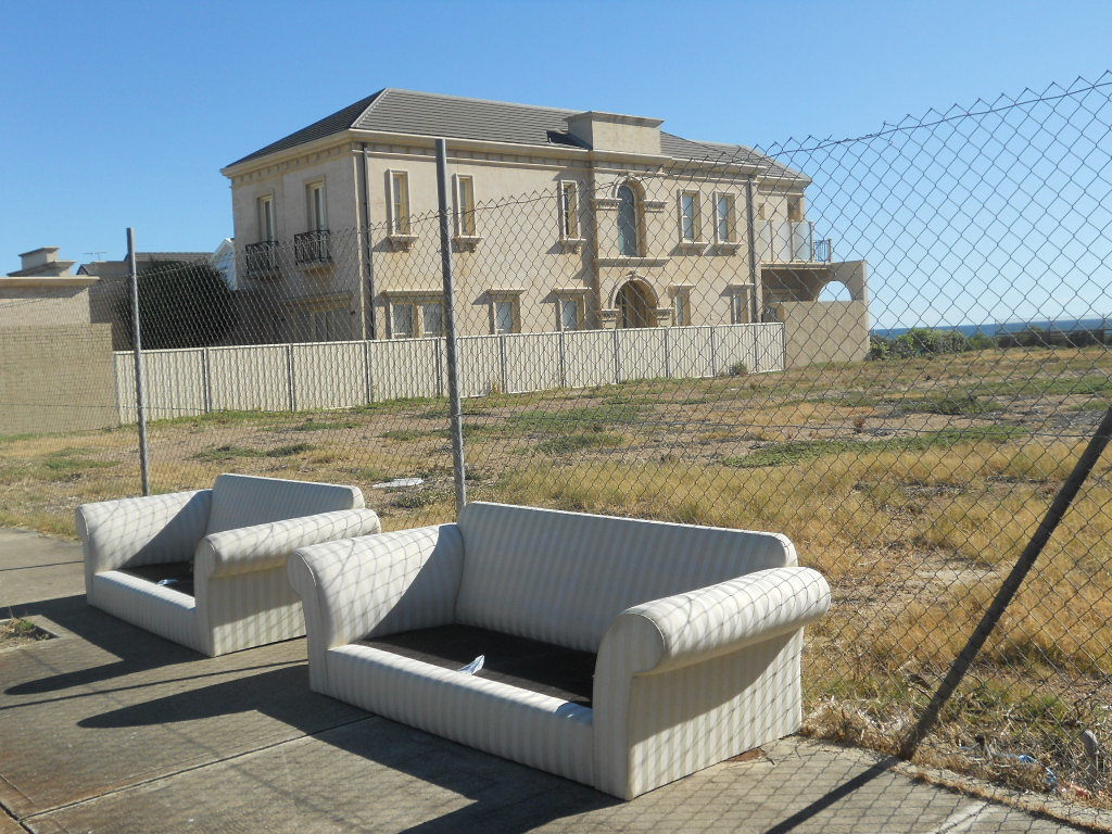 Mansion behind a fence, discarded sofas in trash