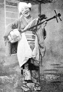 A photograph of a Japanese folkwoman playing shamisen