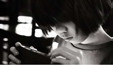 A photograph shows a young person looking at a handheld electronic device.