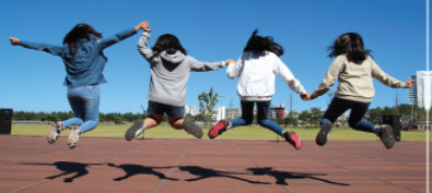 A photograph captures four people midair as they hold hands and jump.