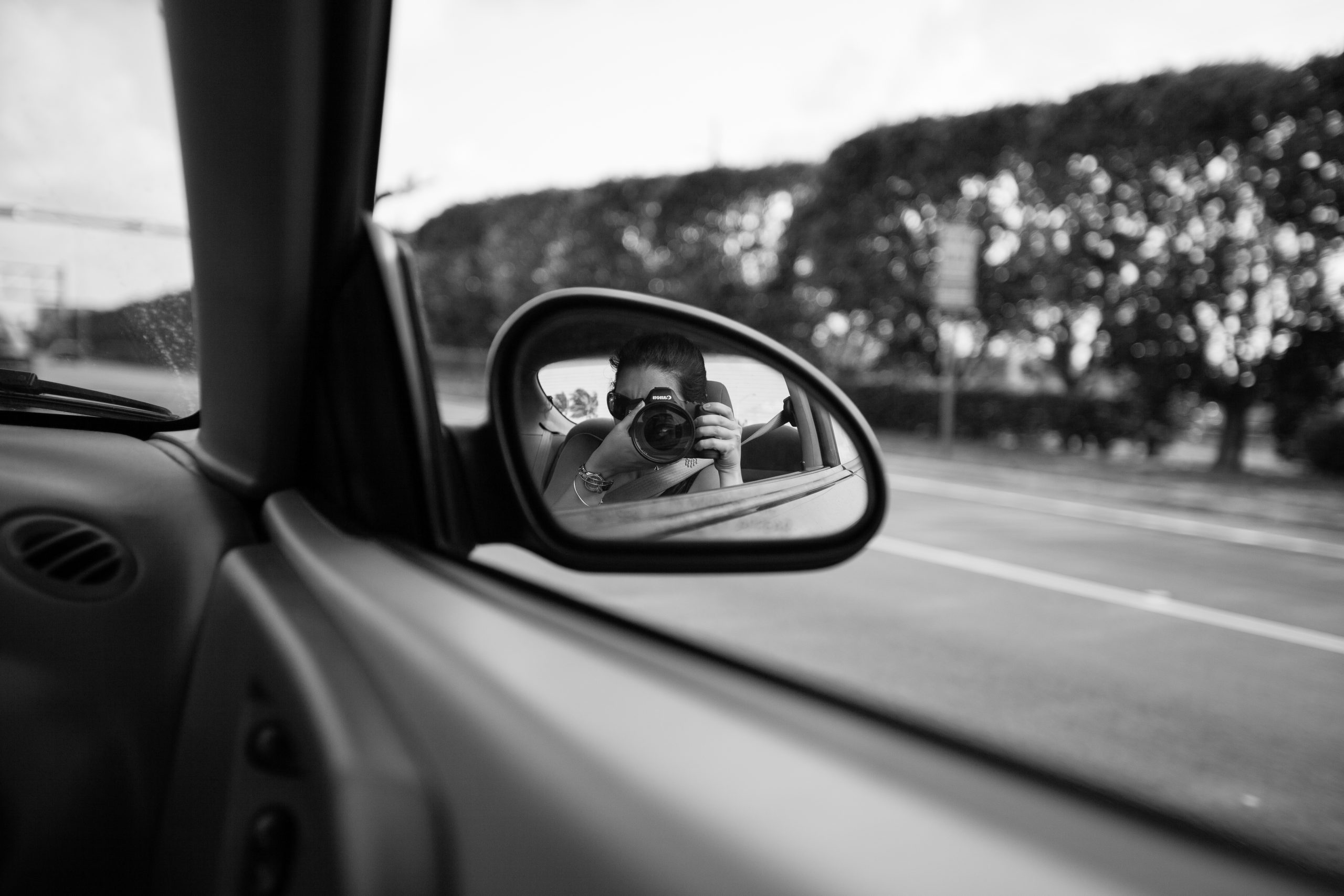 reflection of a photographer taking the photograph in the side-view mirror of a car